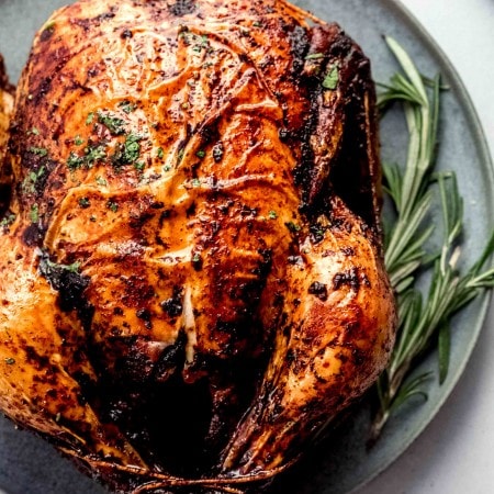 Roasted chicken on grey serving plate with sprig of rosemary.