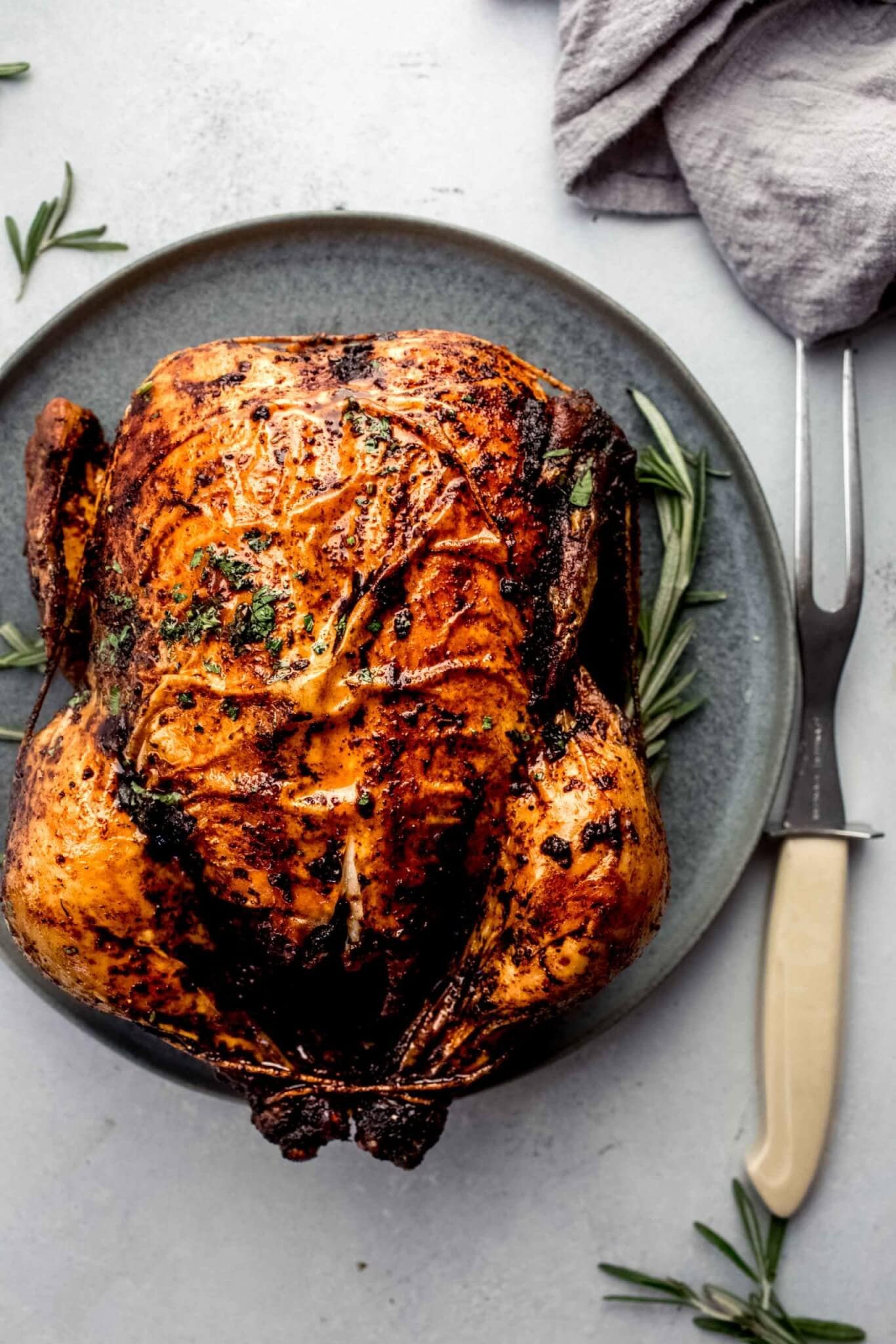 Roasted chicken on grey serving plate with sprig of rosemary and carving fork.