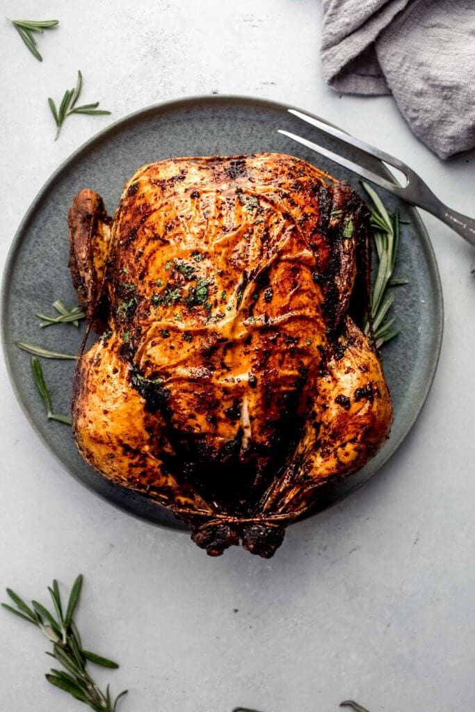 Roasted chicken on grey serving plate with sprig of rosemary and carving fork.