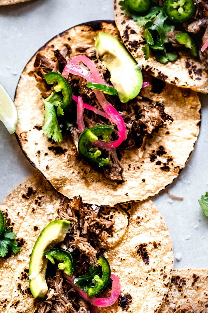 Close up of carnitas taco topped with pickled onion, jalapeno and avocado.