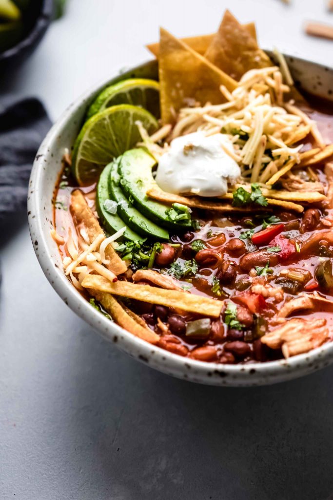 Side view of bowl of tortilla soup topped with avocado, sour cream and tortilla strips. .