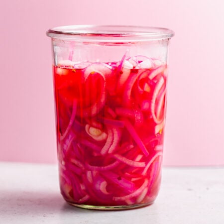 Side shot of jar of pickled onions with pink background.