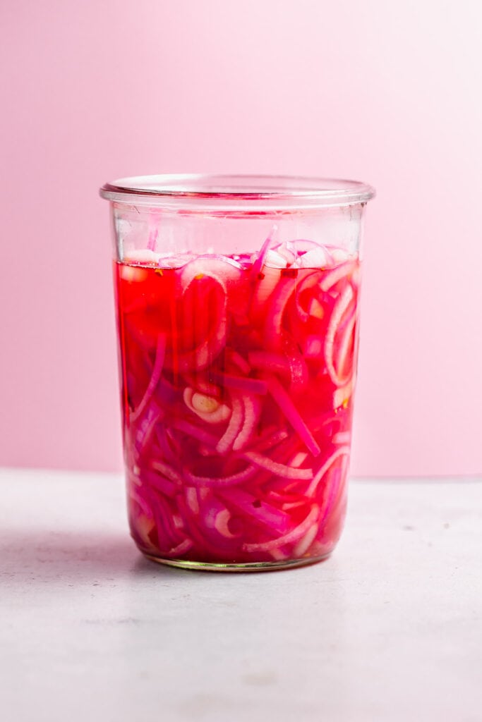 Side shot of jar of pickled onions with pink background.