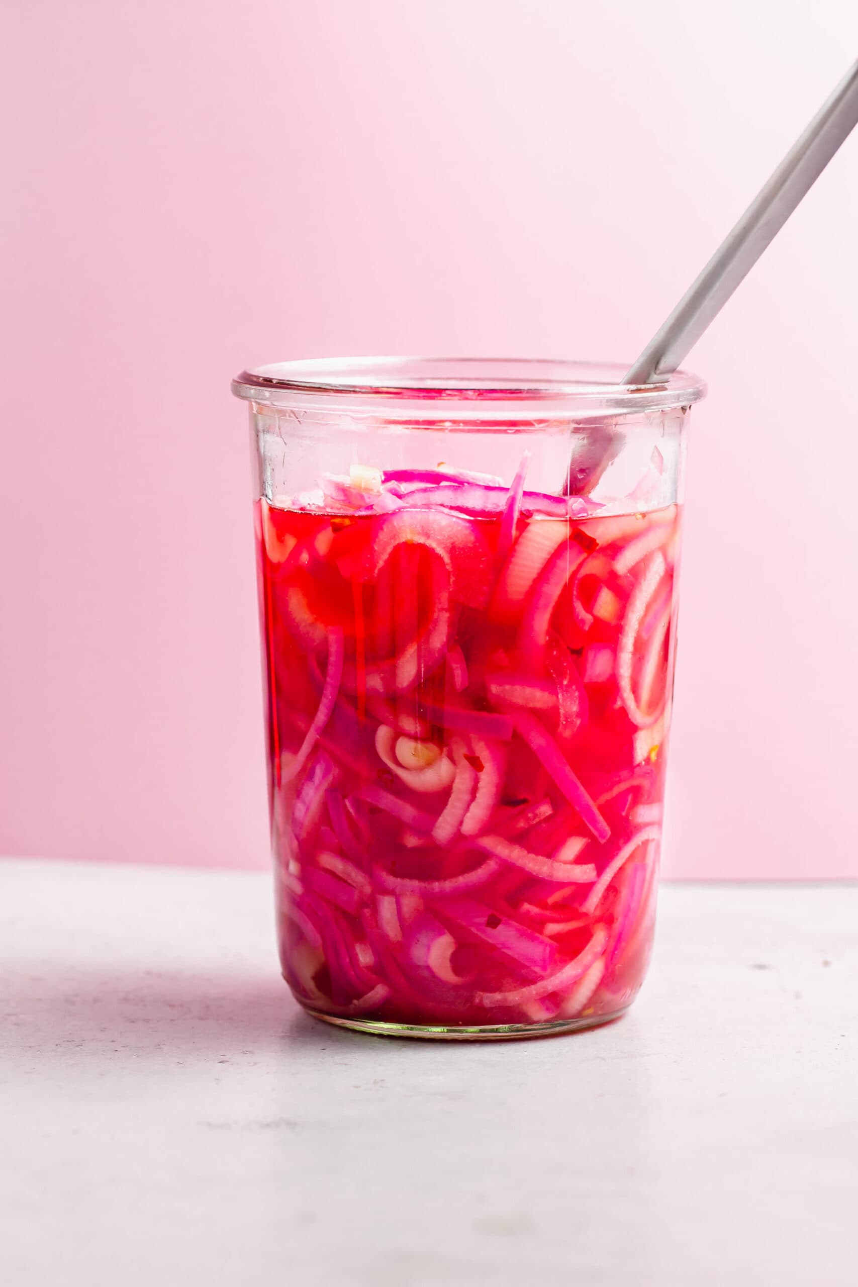 Side view of pickled onions in jar with fork.