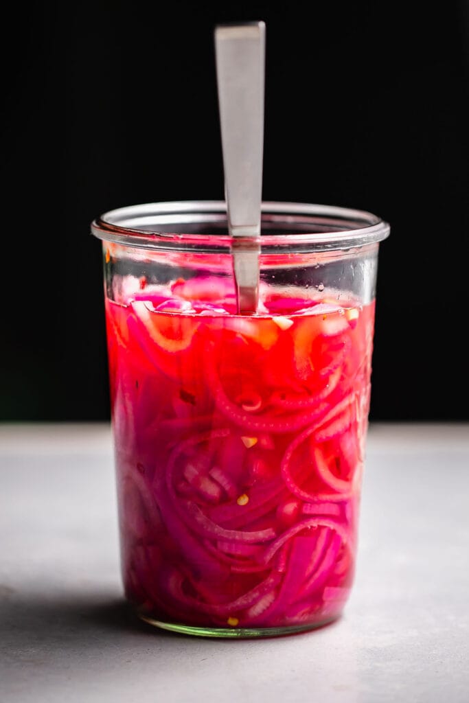Jar of pickled onions with fork on black background. 