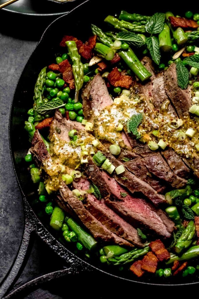 Steak arranged in cast iron skillet with peas and asparagus. 