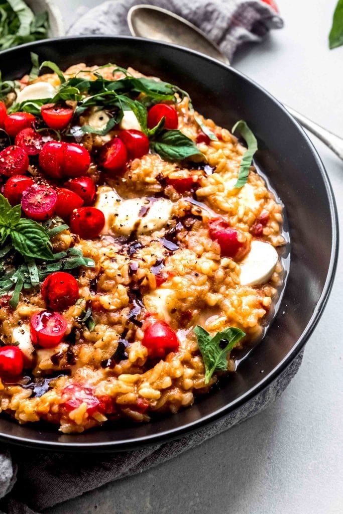 Side view close up of tomato risotto on black plate garnished with fresh basil and balsamic glaze.