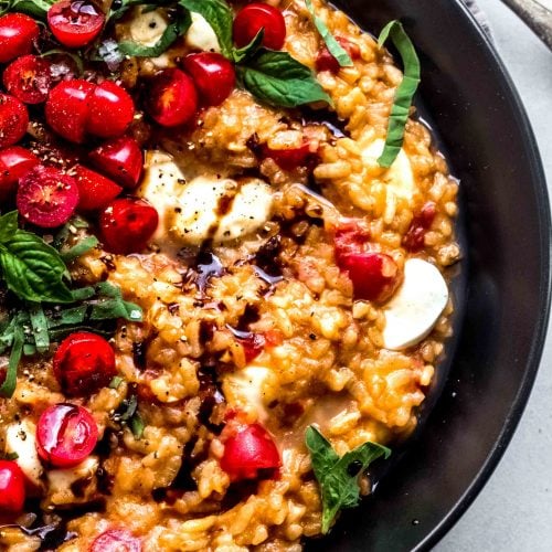 Overhead close up of tomato risotto on black plate garnished with fresh basil and balsamic glaze.