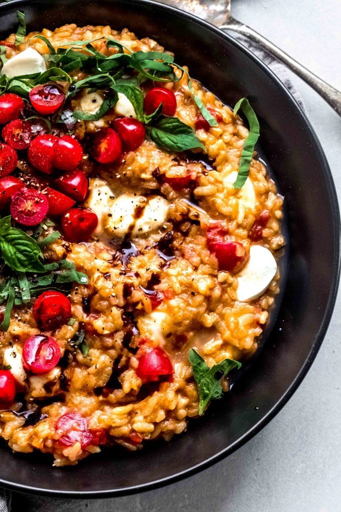 Overhead close up of tomato risotto on black plate garnished with fresh basil and balsamic glaze.