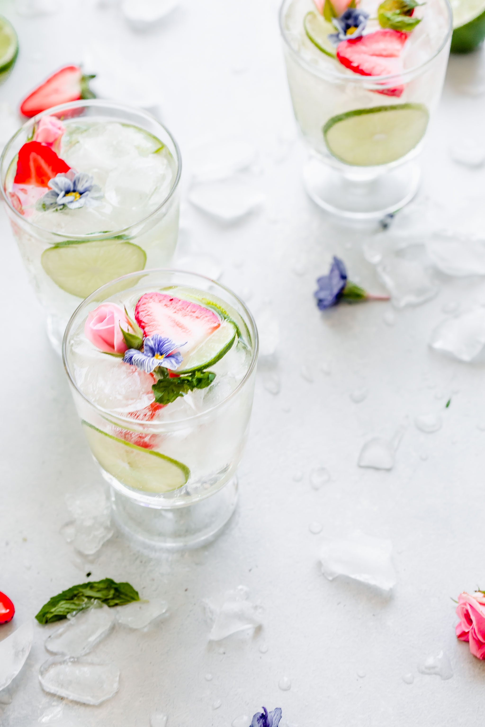 Side view of glass of white wine sangria with purple flowers and strawberries.