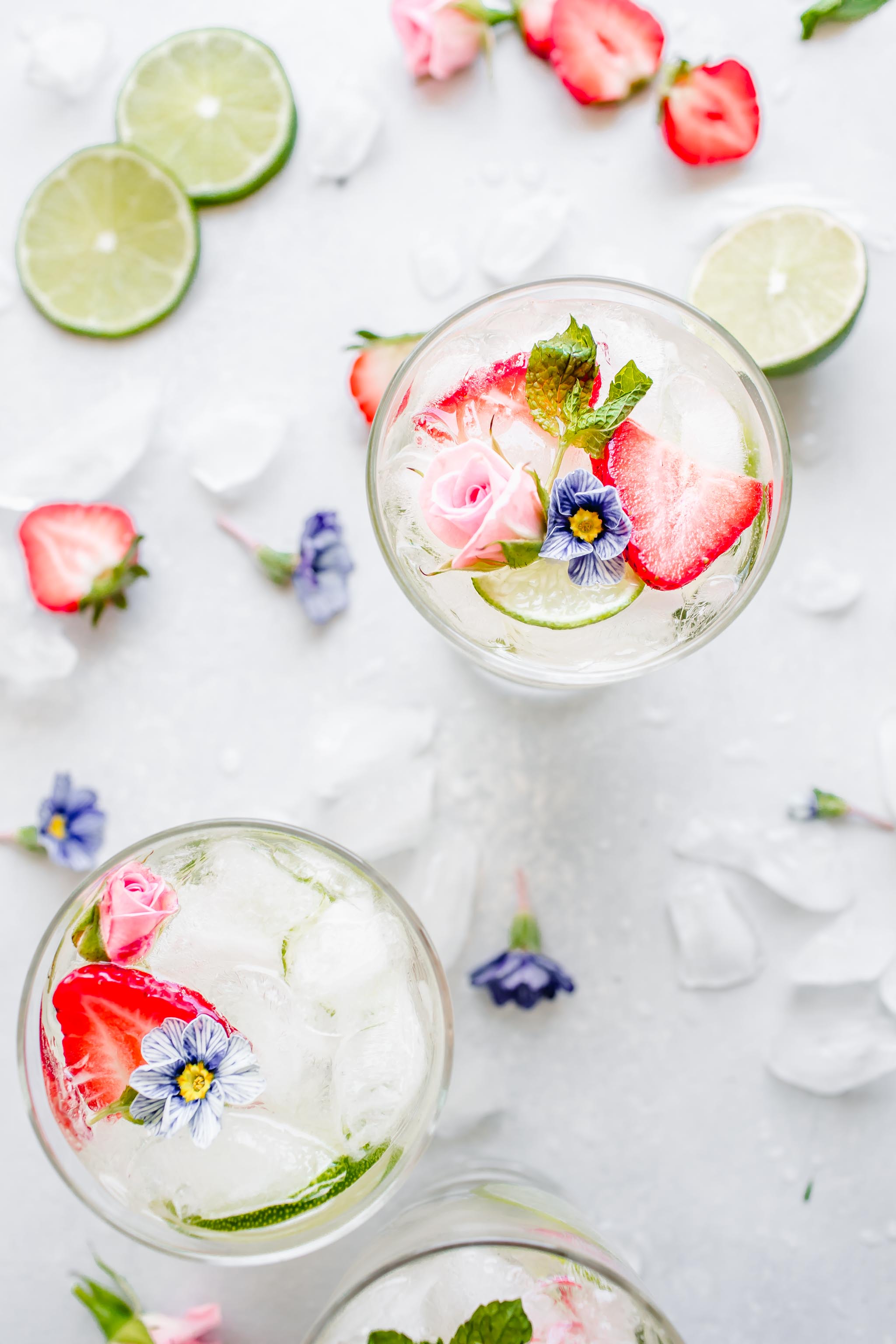 Overhead shot of three glasses of white wine sangria topped with edible flowers.