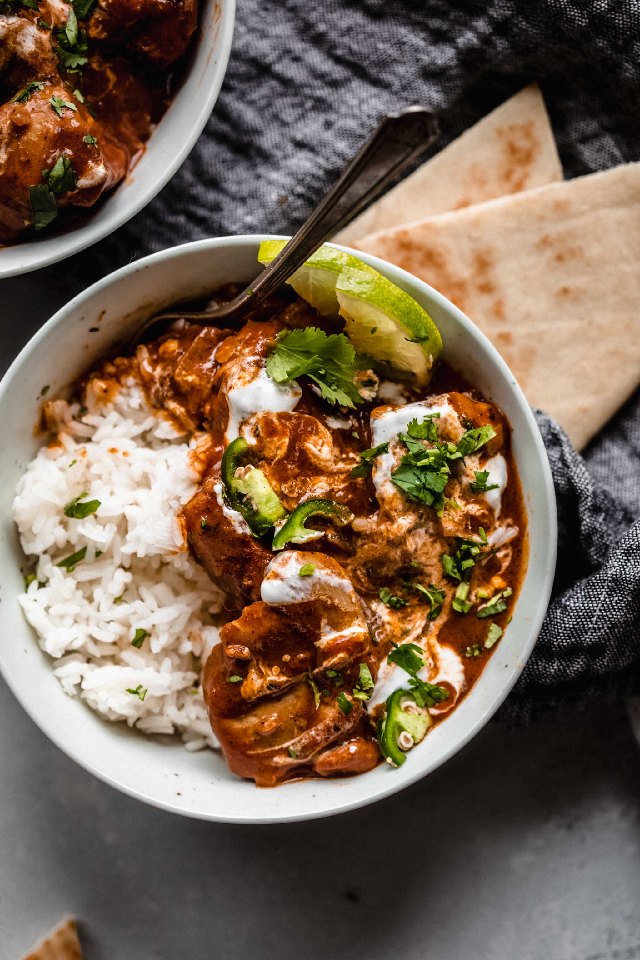 Instant Pot Butter Chicken in bowl served with lime wedges and naan.
