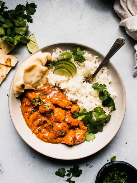 Overhead shot of instant pot butter chicken in white bowl with rice and naan.