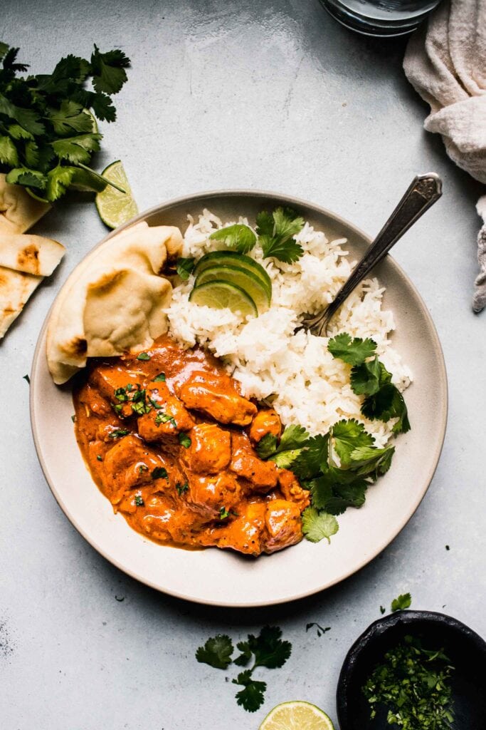 Overhead shot of instant pot butter chicken in white bowl with rice and naan.