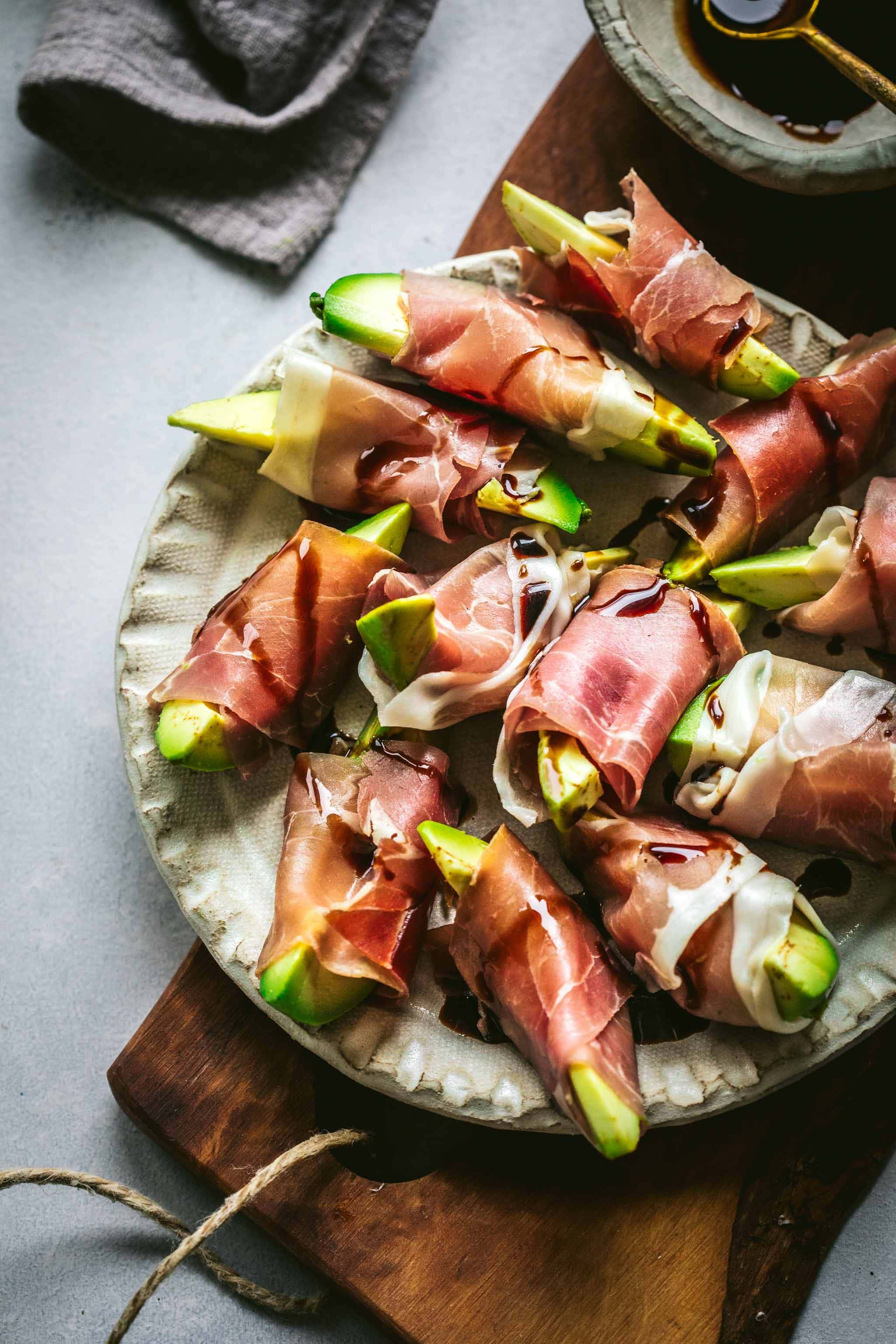 Avocado bites wrapped in prosciutto on wood cutting board.