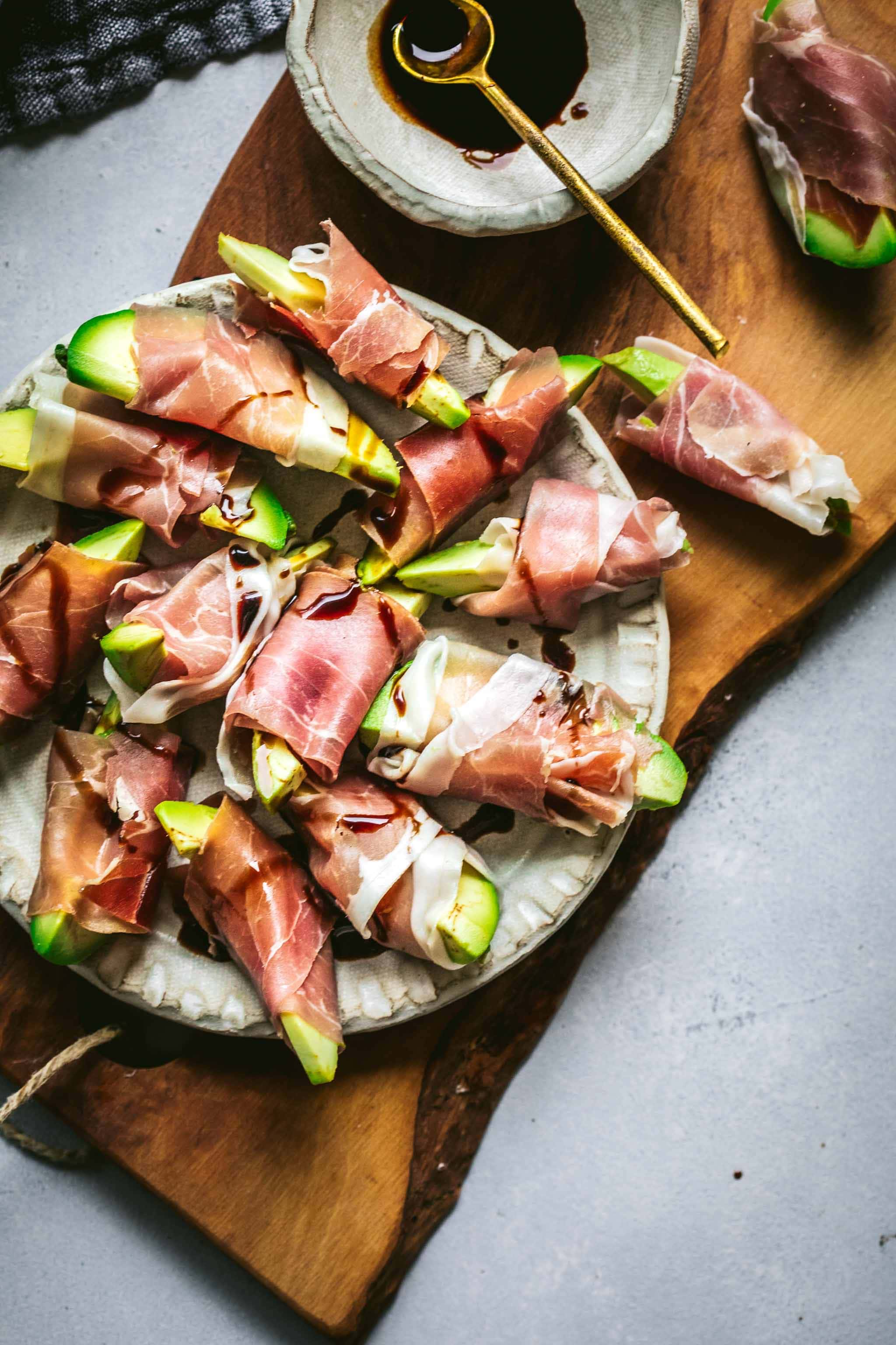 Avocado bites wrapped in prosciutto on wood cutting board.