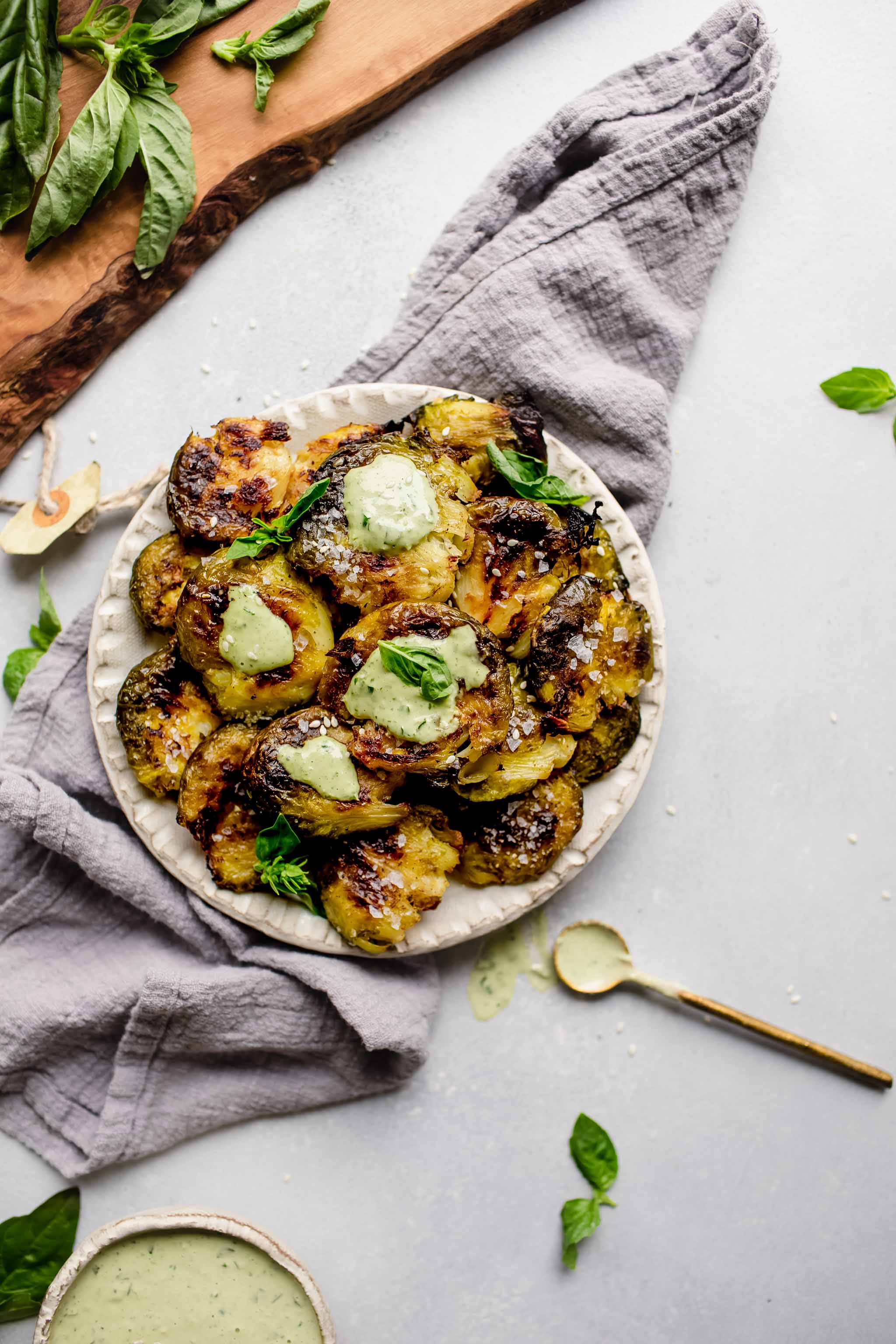 Smashed brussels sprouts on serving plate drizzled with lemon tahini sauce.