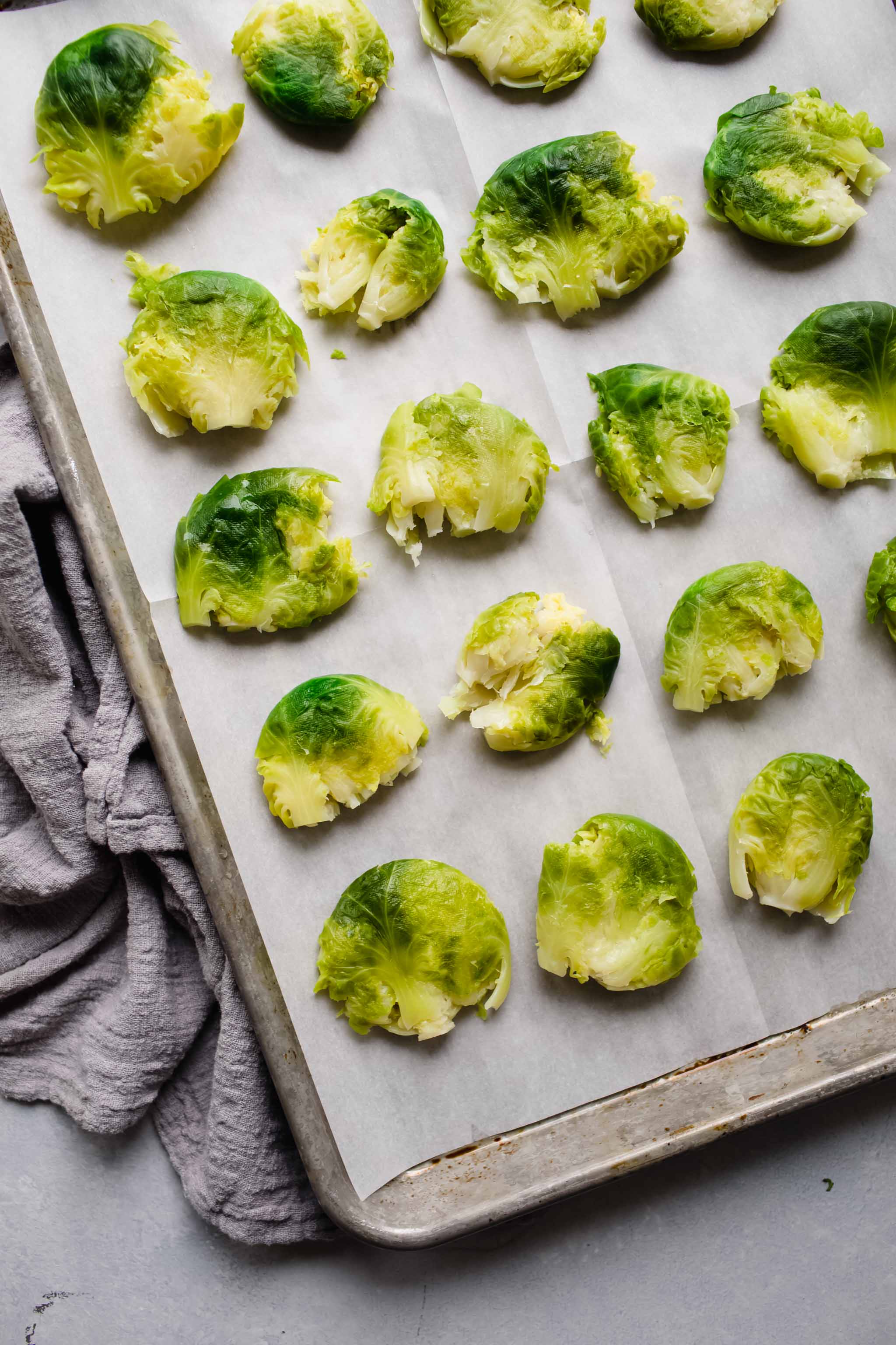 Smashed brussel sprouts arranged on baking sheet ready for oven. 