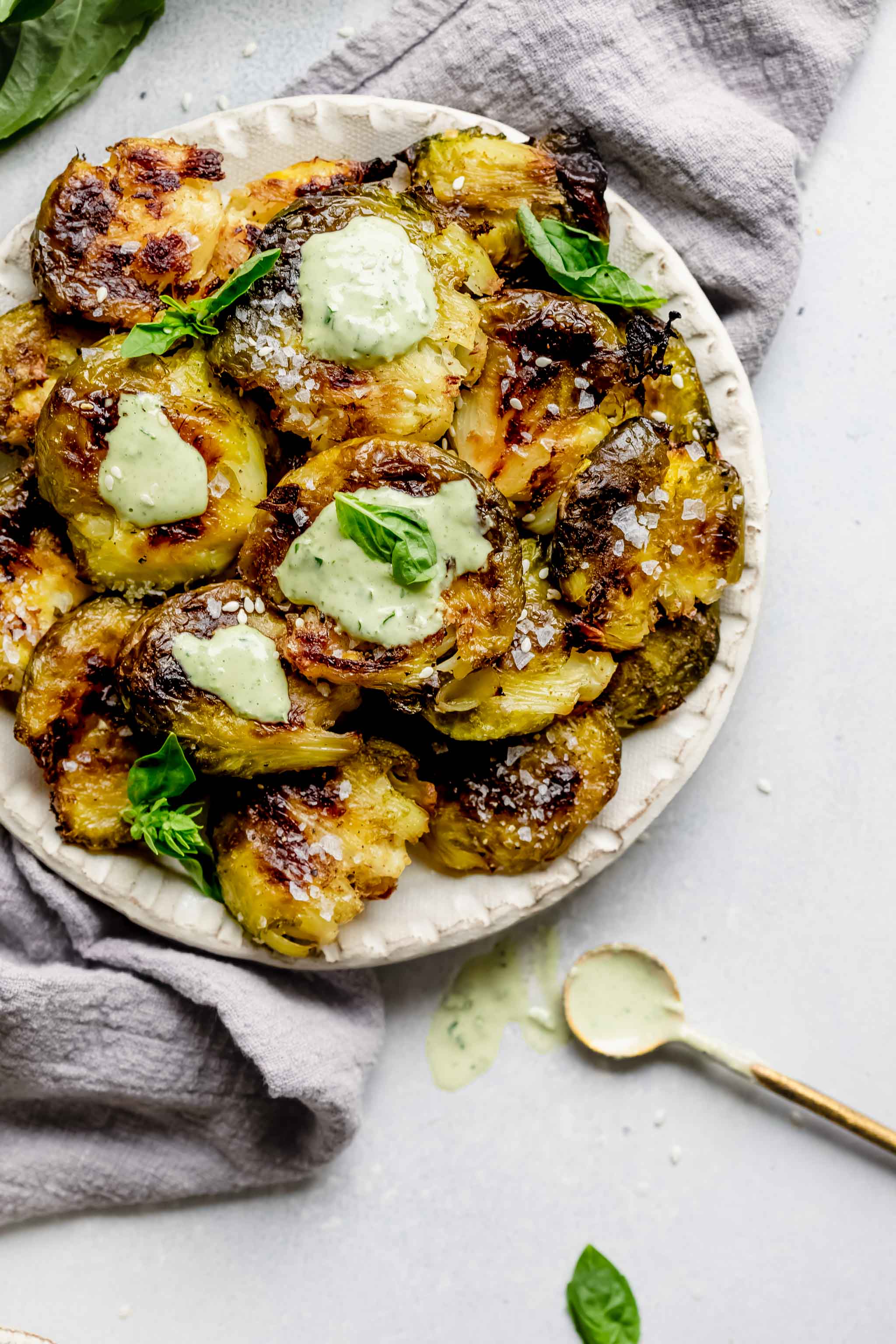 Smashed brussel sprouts on serving plate drizzled with lemon tahini sauce. 