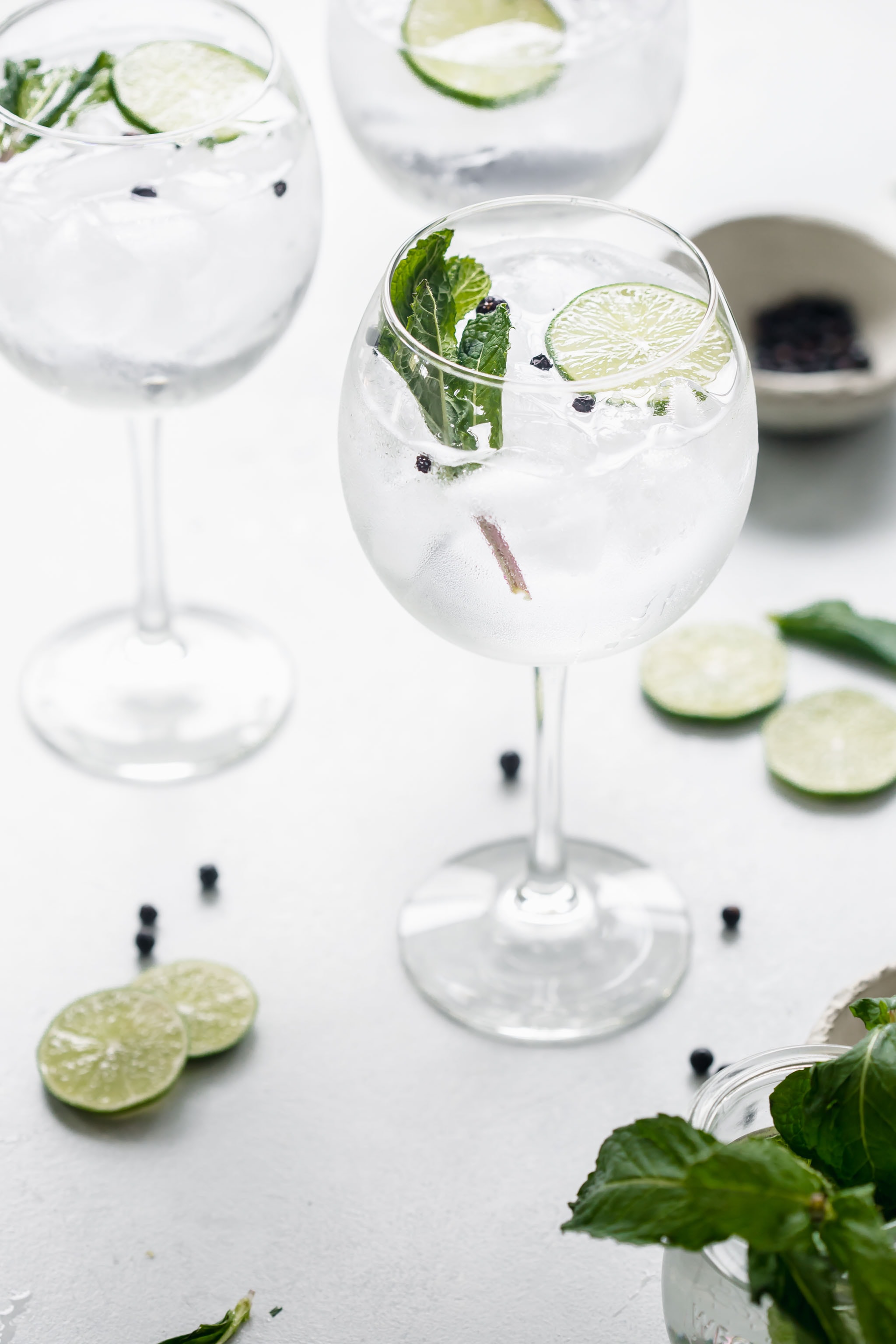 Three gin and tonics arranged on table next to lime wedges.