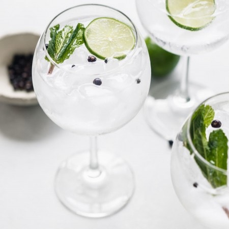 Three glasses of gin tonic cocktail garnished with limes and mint.
