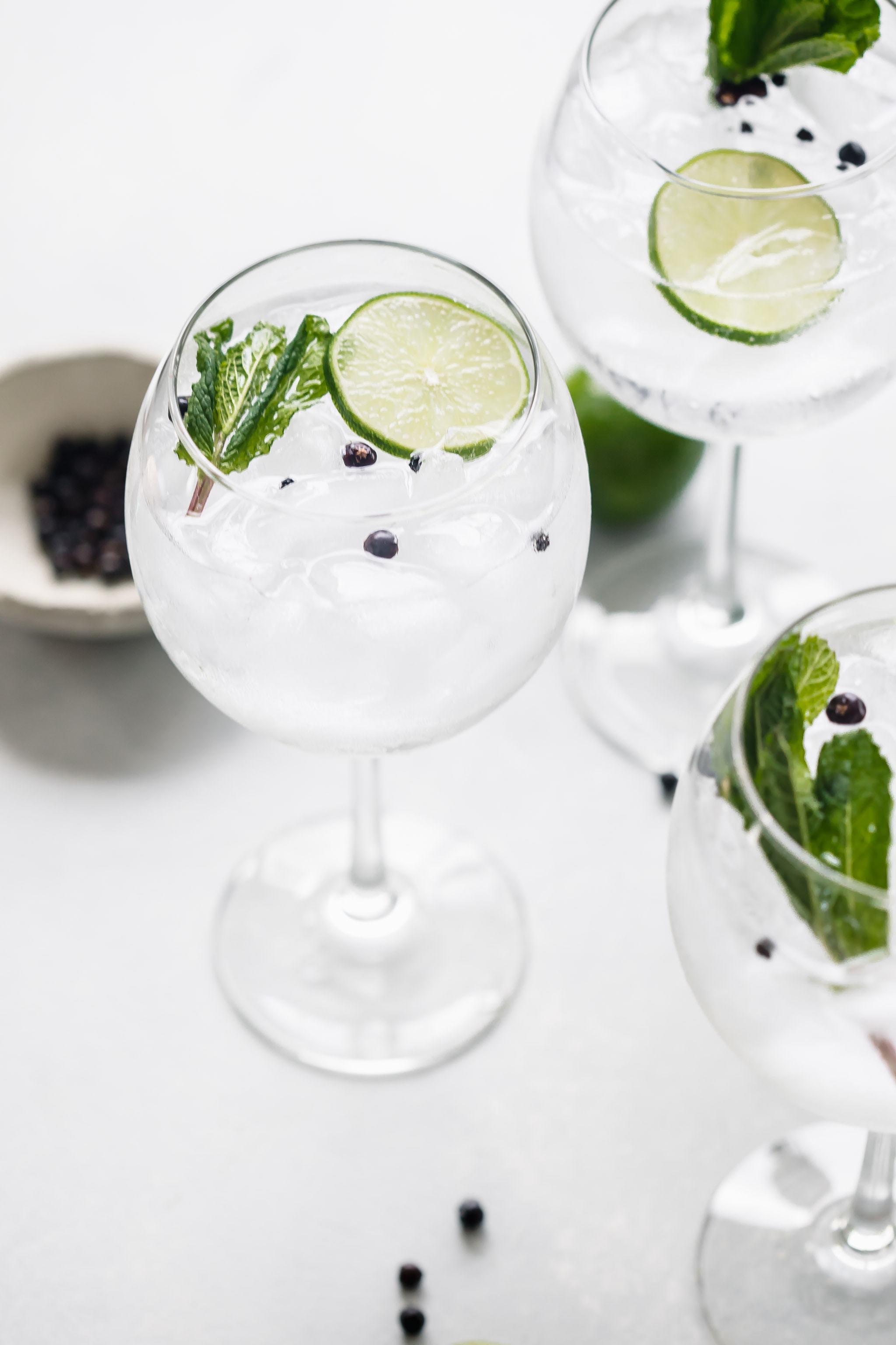 Three glasses of gin tonic cocktail garnished with limes and mint.