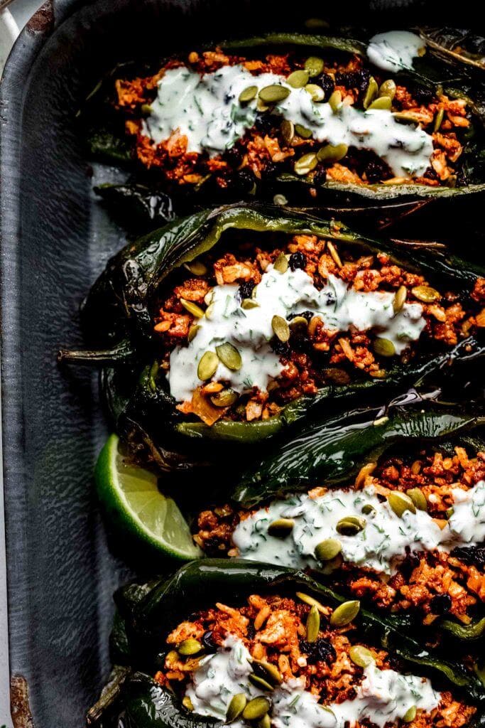 Overhead shot of stuffed poblanos arranged in baking dish drizzled with lime crema.