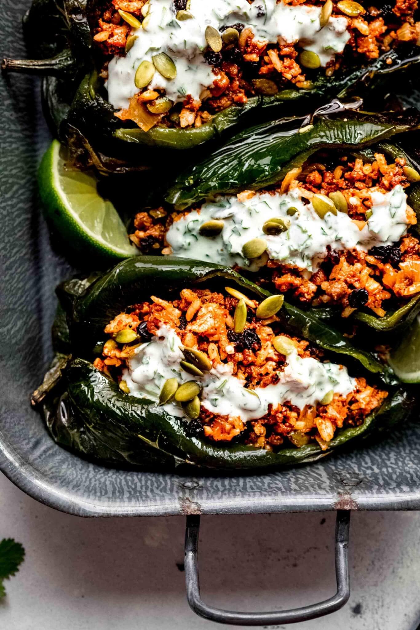 Stuffed poblano peppers in serving dish drizzled with crema.
