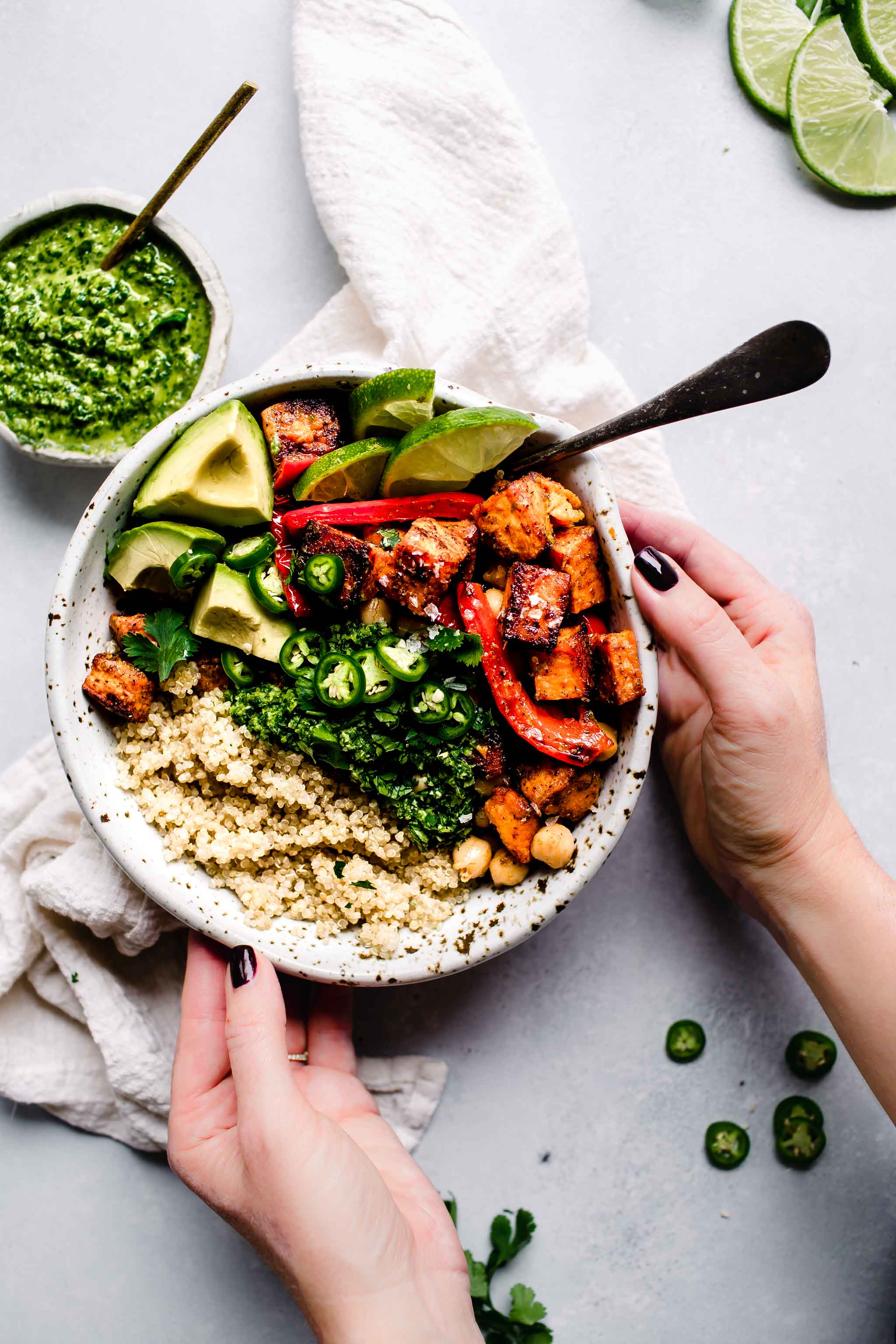Two hands holding bowl of quinoa topped with peppers, sweet potatoes, chickpeas, avocado and drizzled with mojo sauce.