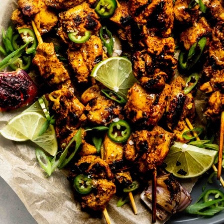 Close up of curry chicken skewers on grey plate with parchment paper.