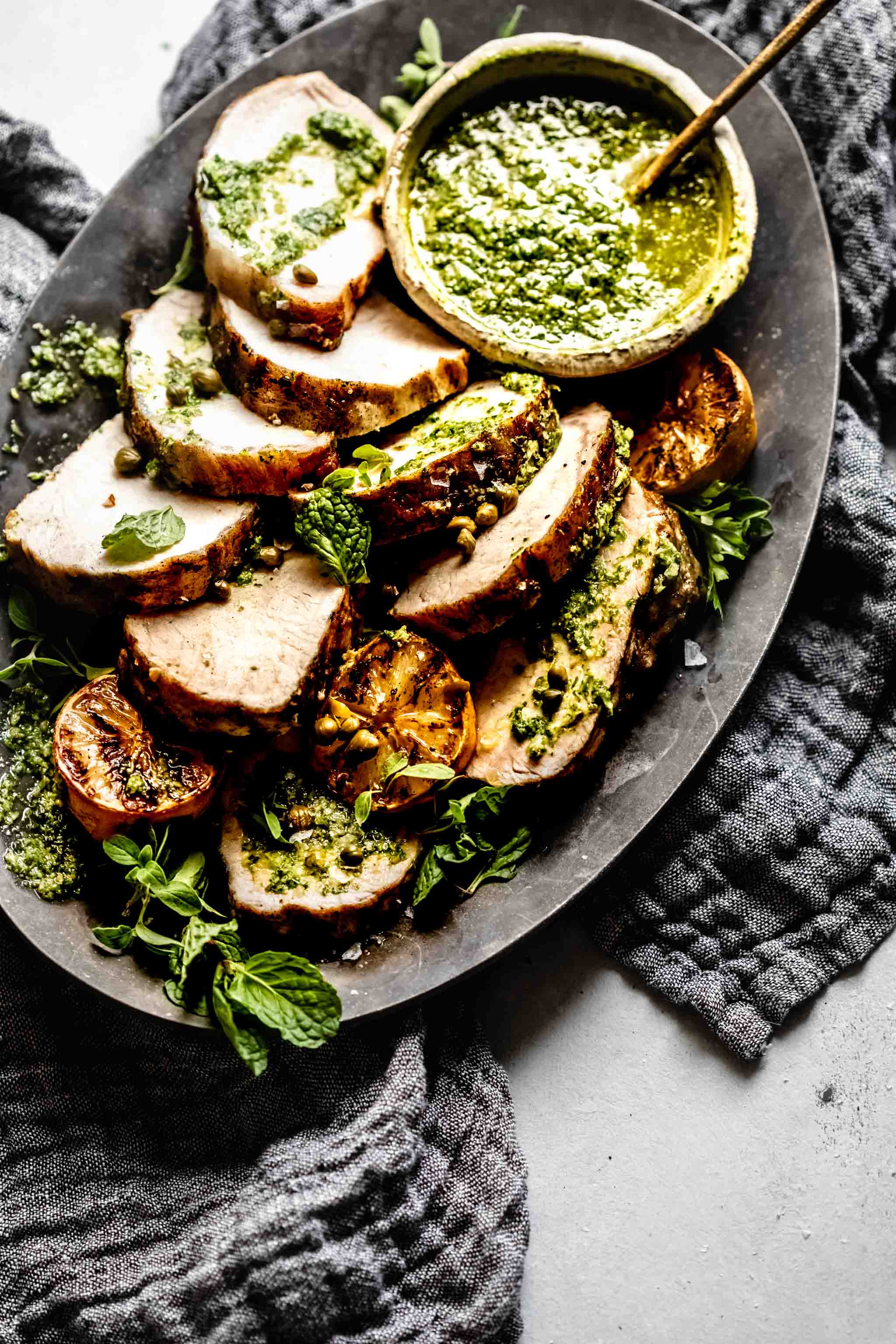 Slices of grilled pork tenderloin on plate drizzled with charred lemon chimichurri.