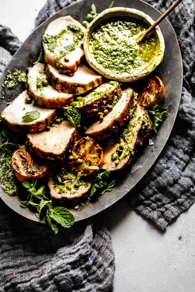 Pork tenderloin slices arranged on tray with chimichurri. 