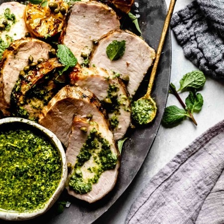 Slices of grilled pork tenderloin on plate drizzled with charred lemon chimichurri.