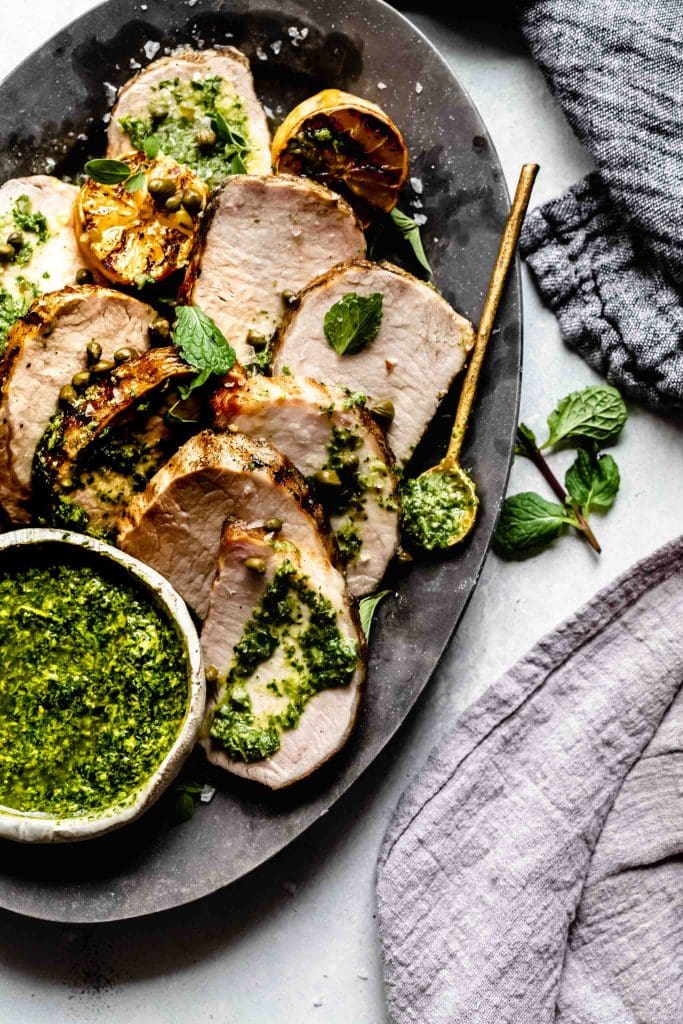 Slices of grilled pork tenderloin on plate drizzled with charred lemon chimichurri.