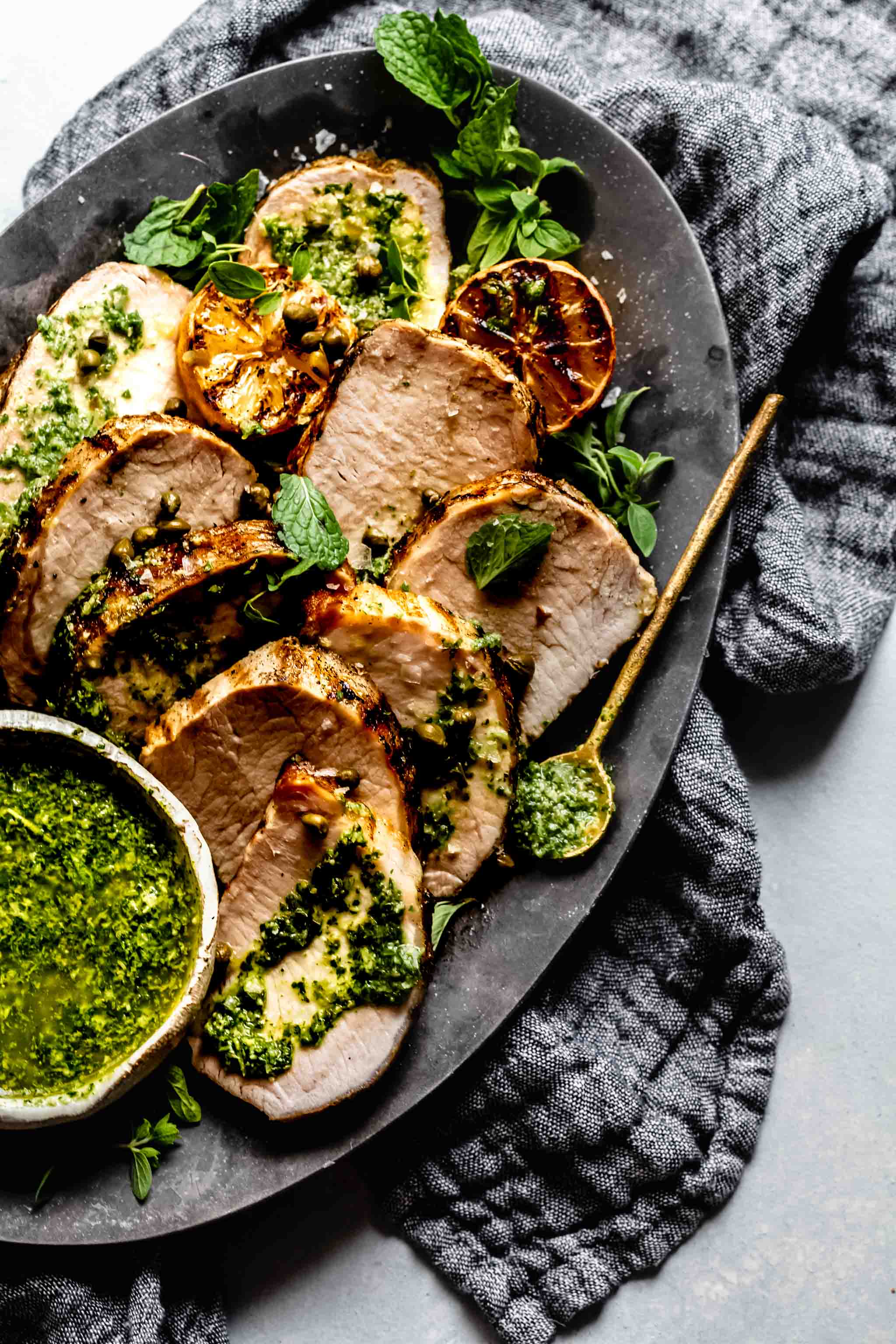 Slices of grilled pork tenderloin on plate drizzled with charred lemon chimichurri.