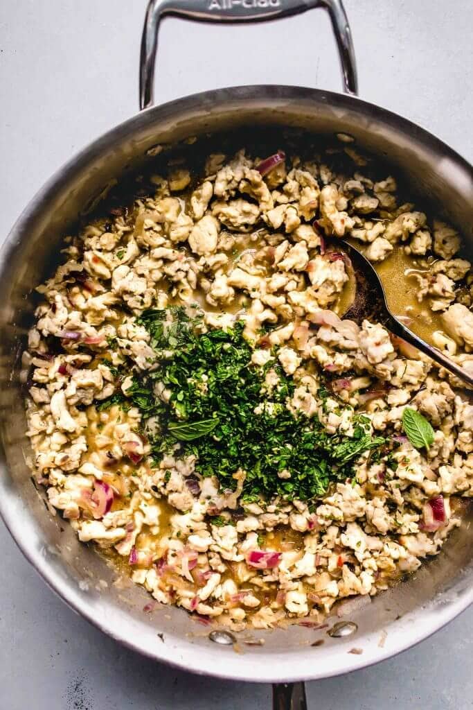 Cooked ground chicken in skillet with fresh herbs. 