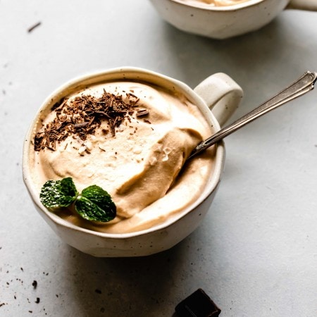 Side view of two mugs of coffee mousse topped with chocolate shavings and mint sprigs.