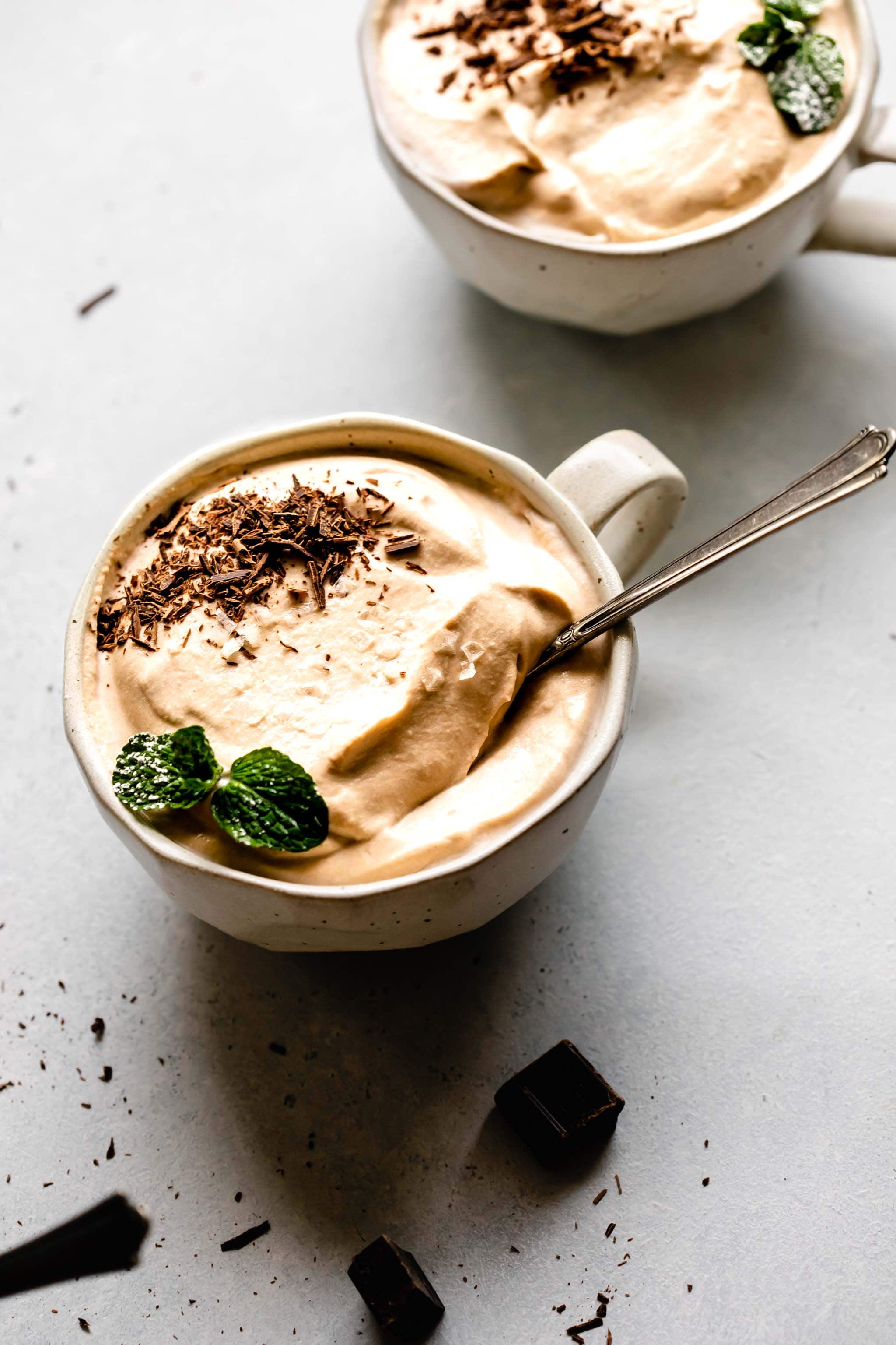 Side view of two mugs of coffee mousse topped with chocolate shavings and mint sprigs.