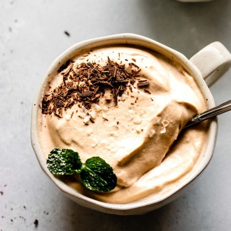 Overhead close up of bowl of coffee mousse topped with flaky salt, mint sprig and chocolate shavings.