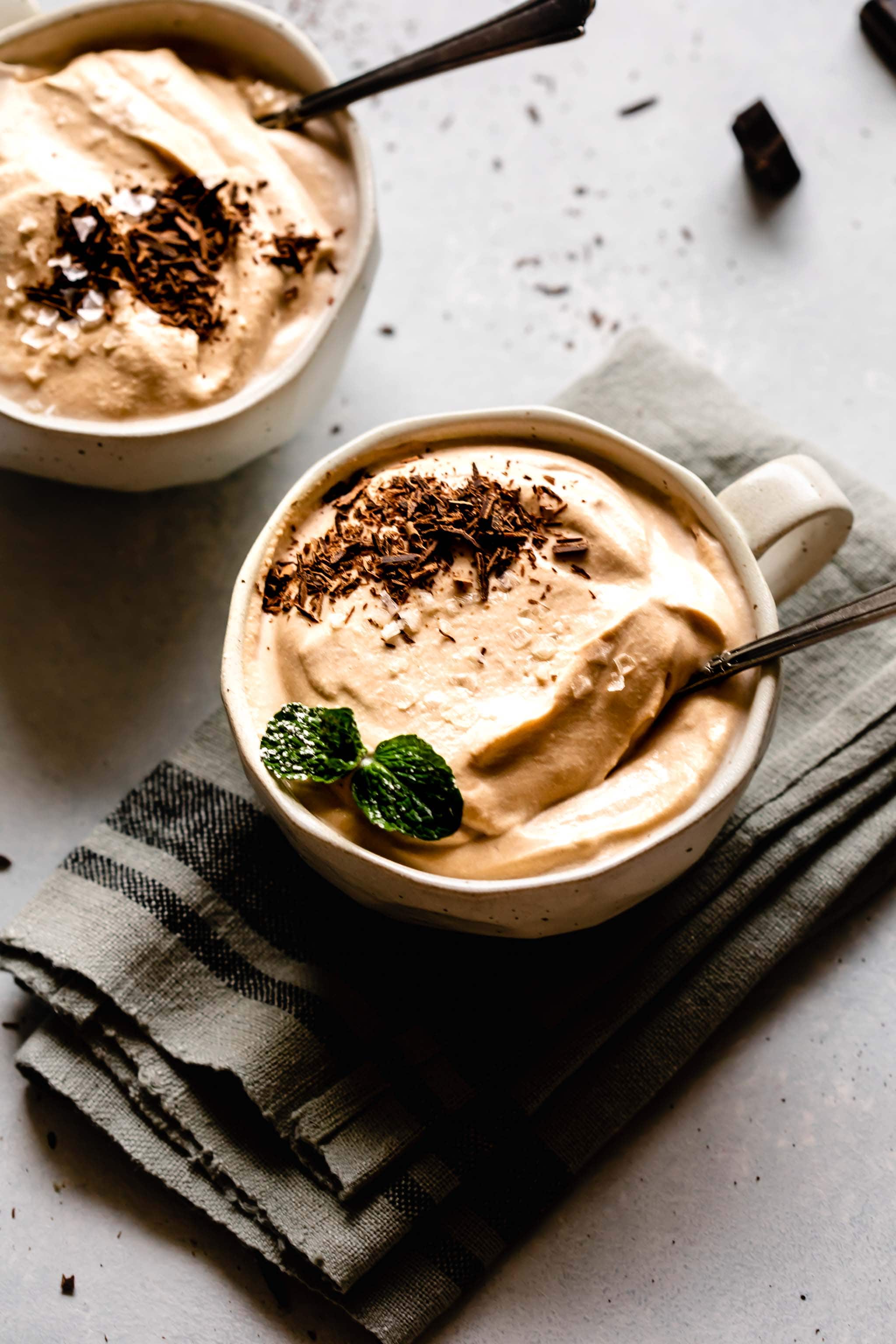 Side view of two mugs of coffee mousse topped with chocolate shavings and mint sprigs.