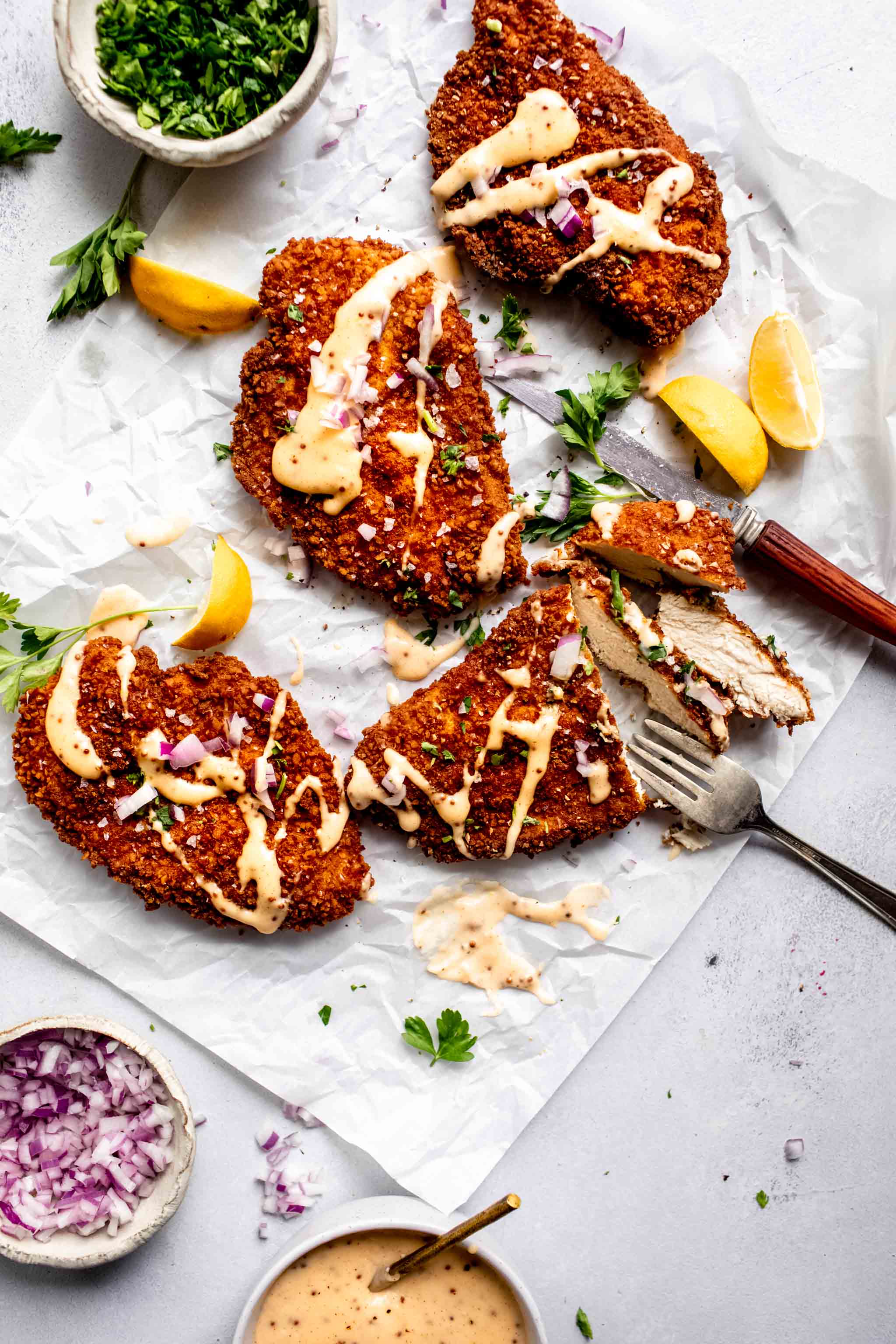 Four pretzel crusted chicken cutlets on piece of parchment drizzled with cheddar mustard sauce.