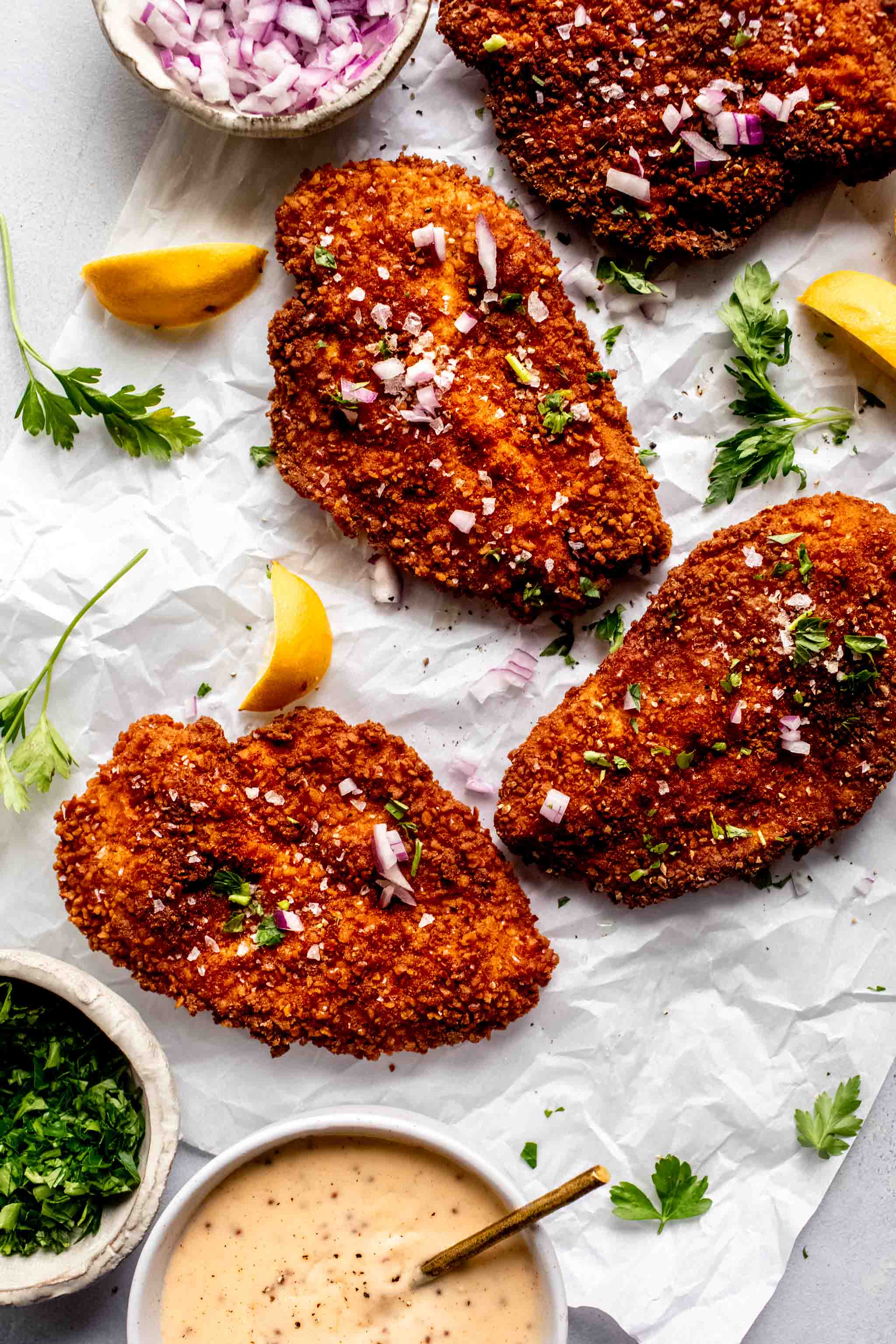 Pretzel coated chicken breasts on piece of parchment before drizzling with cheese sauce.