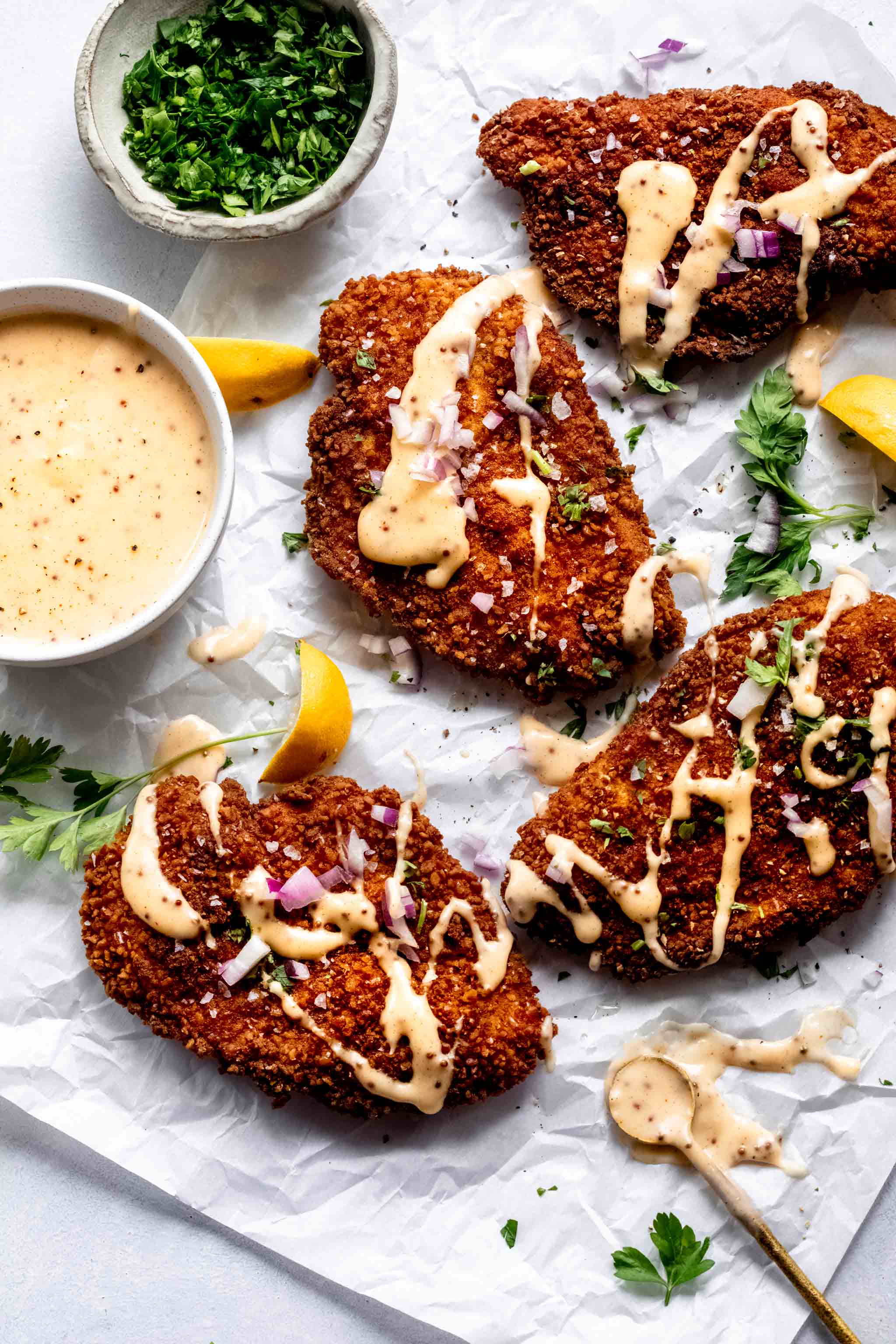 Four pretzel crusted chicken cutlets on piece of parchment drizzled with cheddar mustard sauce.