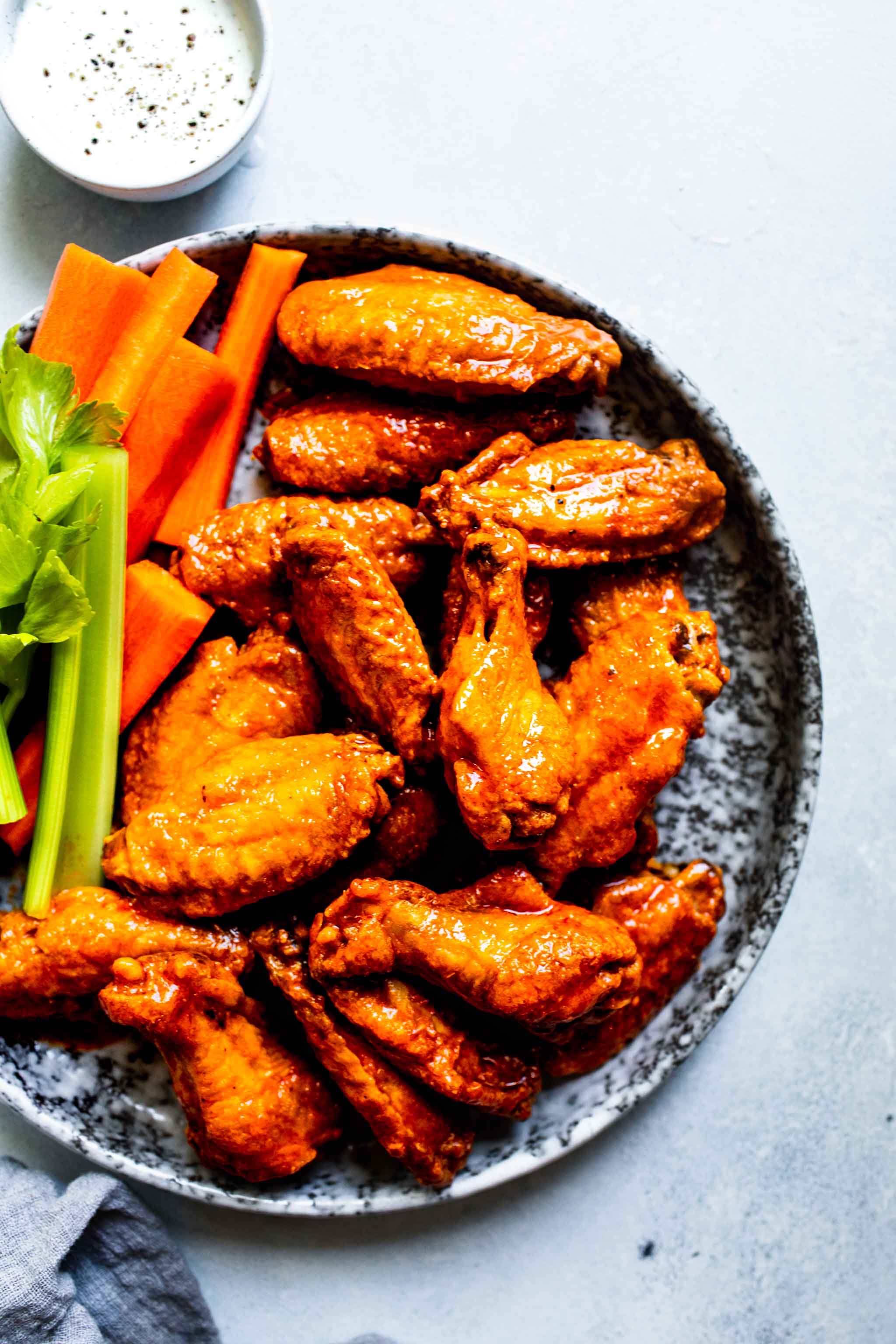Baked buffalo wings coated in buffalo sauce on grey speckled plate next to blue cheese and celery sticks.