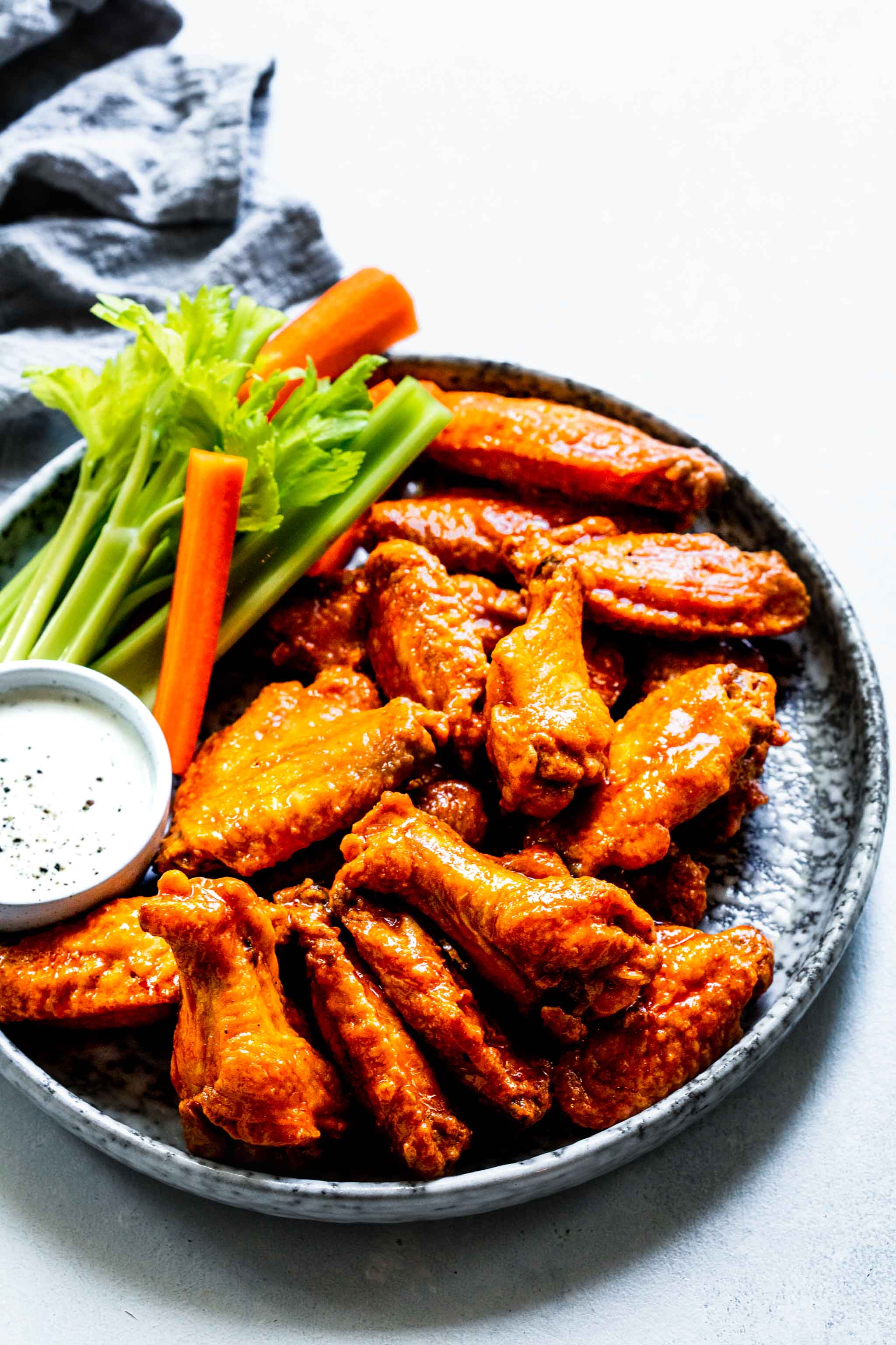 Baked buffalo wings coated in buffalo sauce on grey speckled plate next to blue cheese and celery sticks.