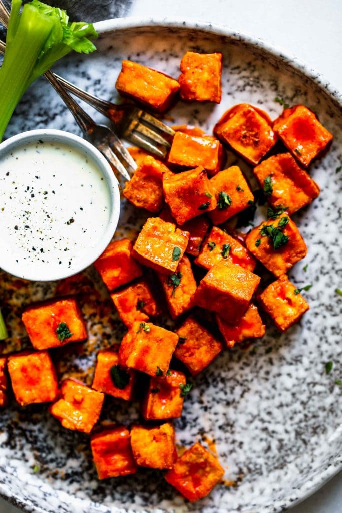 Buffalo tofu bites on grey speckled plate next to side of blue cheese and celery.