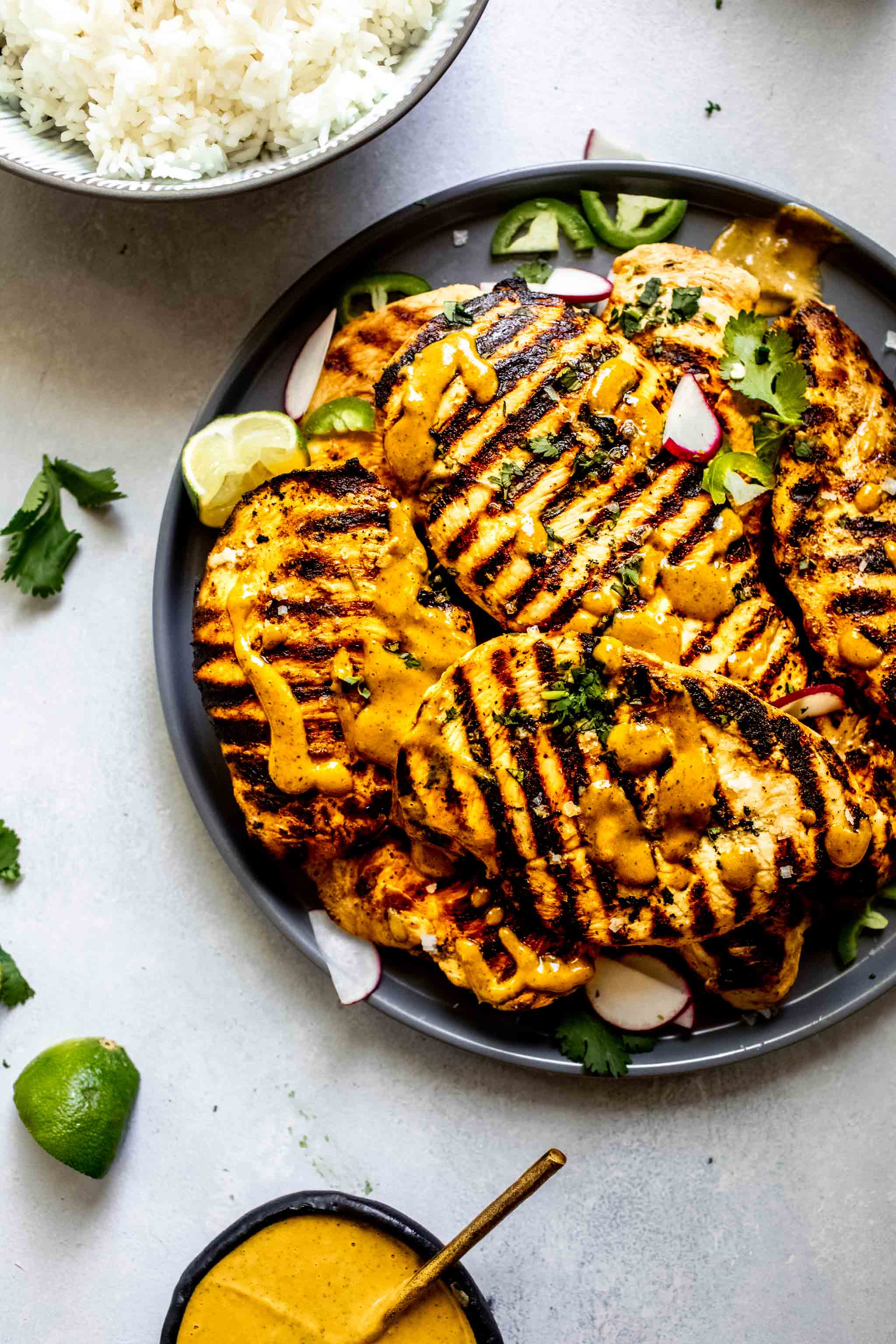Grilled chicken breasts on grey plate drizzled with spicy peanut sauce.