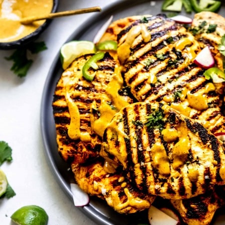 Grilled chicken breasts on grey plate drizzled with spicy peanut sauce.