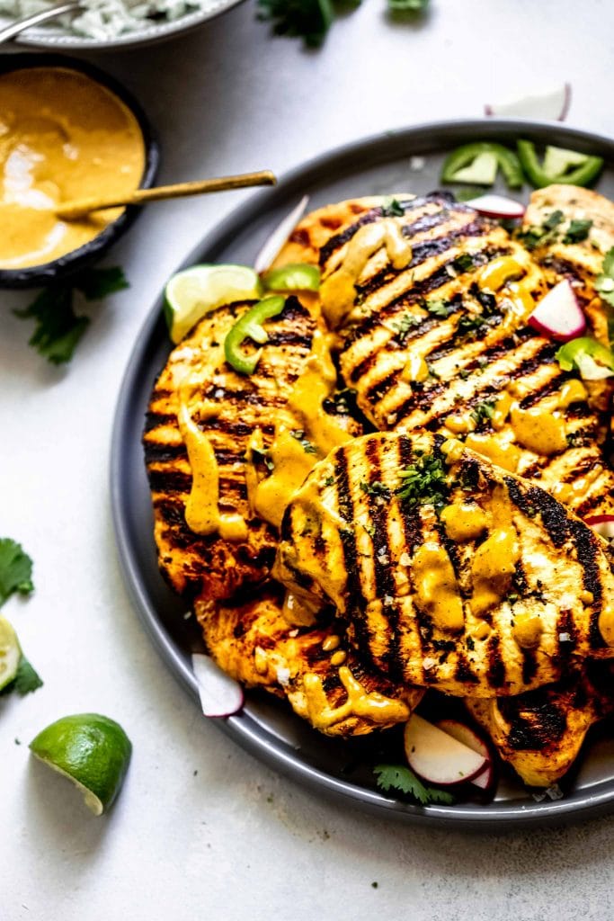 Grilled chicken breasts on grey plate drizzled with spicy peanut sauce.