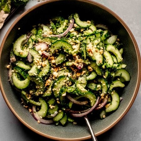 Overhead shot of Thai Cucumber Salad in green bowl with spoon next to bunch of cilantro.